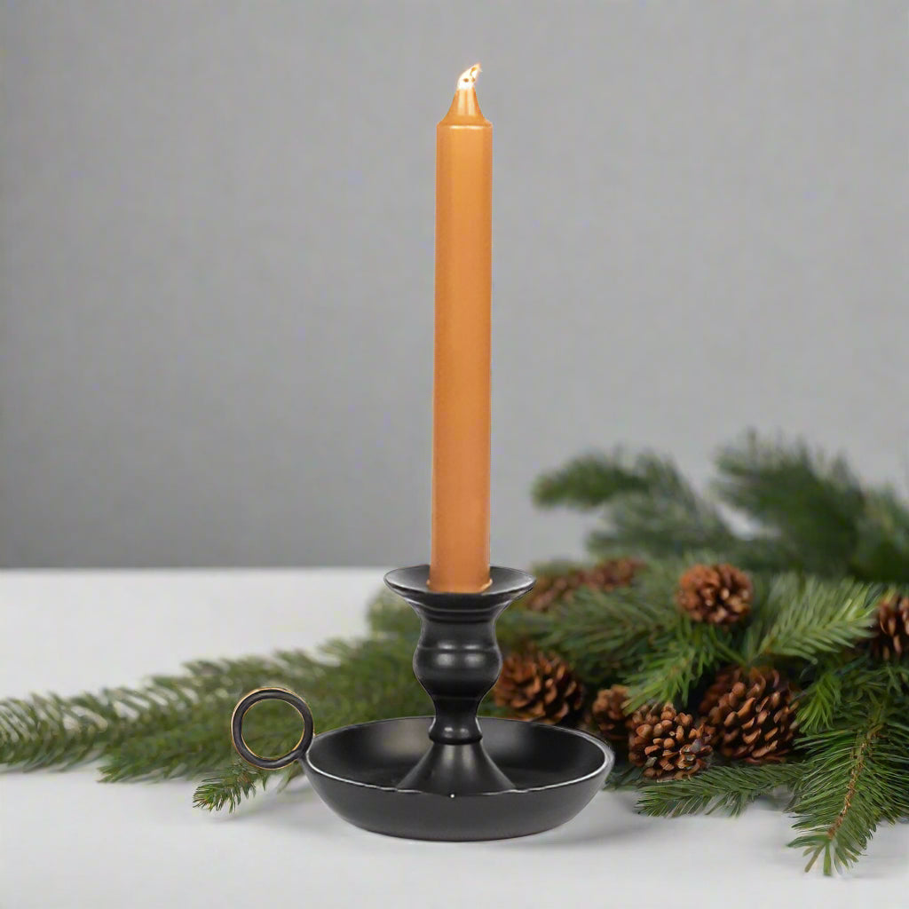 A black metal candle holder with a cylindrical base and a simple design, featuring a candle lit inside.