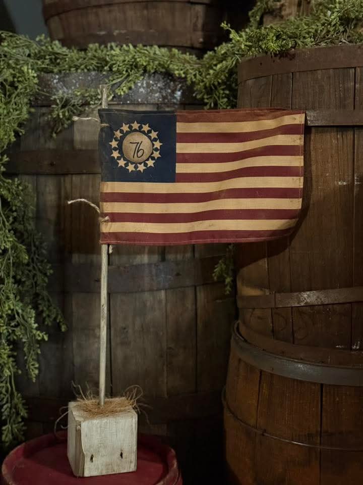 Vintage-style American flag with a decorative emblem on wooden barrels and greenery.