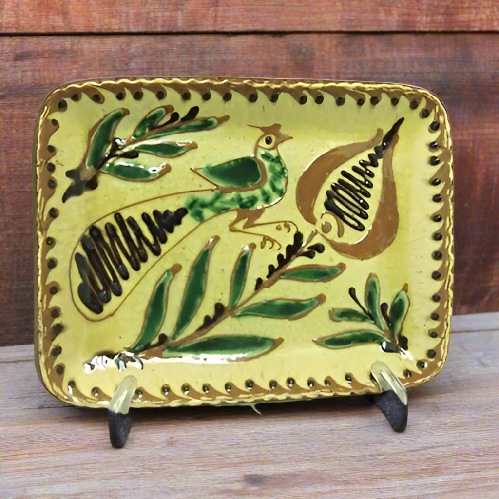 Redware plate in rectangular shape with a bird perched on a flower glazed in yellow, brown and green