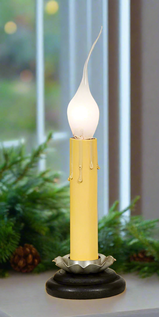 A black candle holder with a lit candle, the holder appears to be made of metal with a matte finish shown in a window sill with greenery.