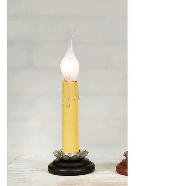 A black candle holder with a lit candle, the holder appears to be made of metal with a matte finish shown in a window sill with greenery.