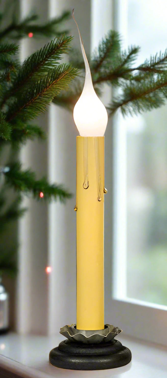 Black base window candle with cream sleeve and a silicone candelabra bulb show on a window sill with greenery beside it