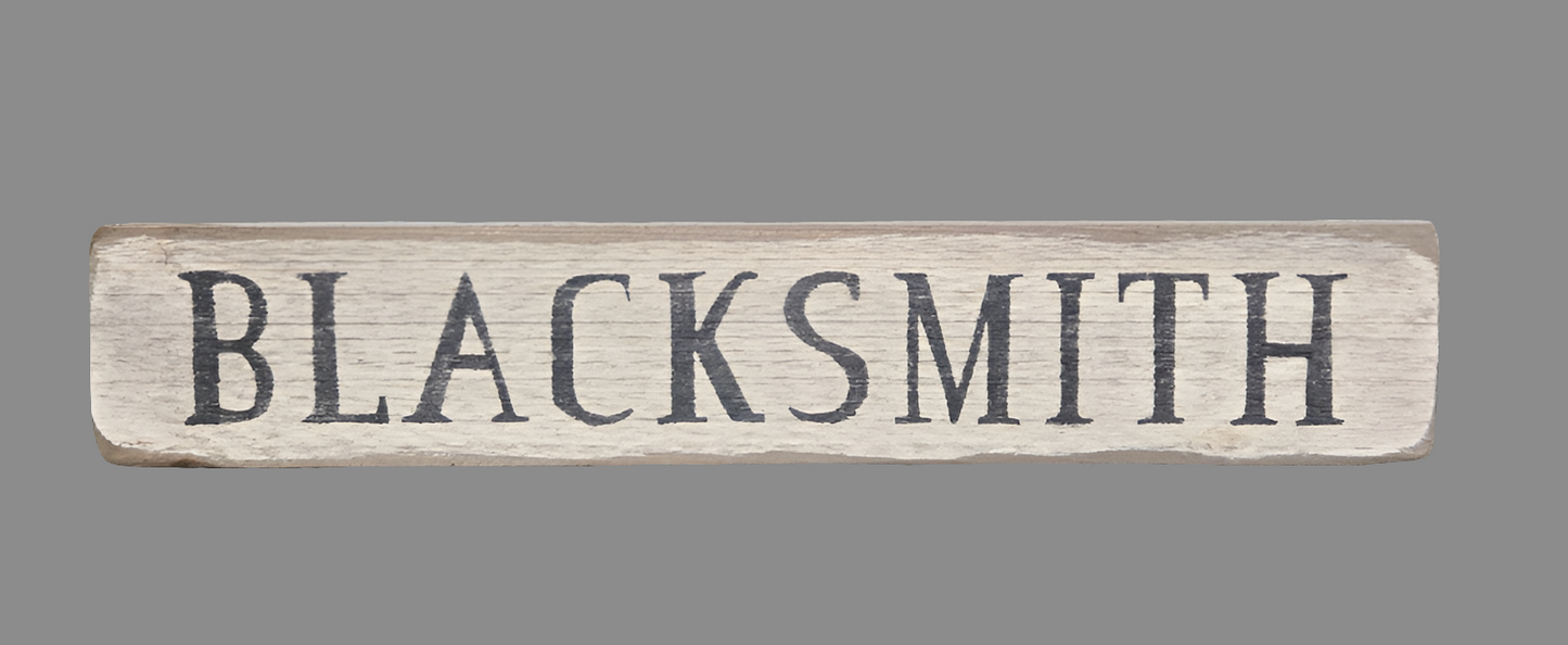 Weathered cream wood sign with the word "Blacksmith" written in black paint