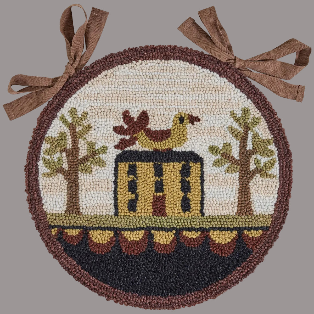A round chair pad with a 'Bless Our Home' design, featuring an artistic representation of a house, trees, and a chicken, in a hooked rug style.