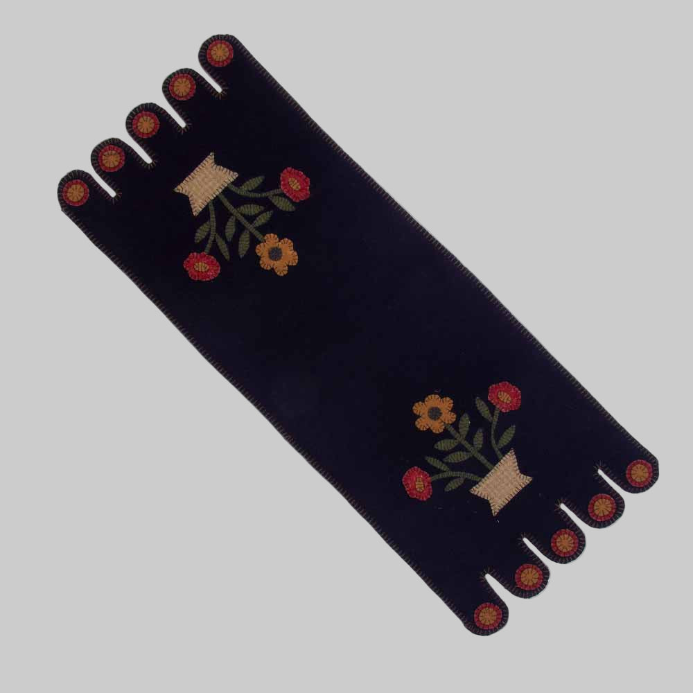 A black table runner with a floral design in mustard and red colors, featuring embroidered flowers and a fringed edge.