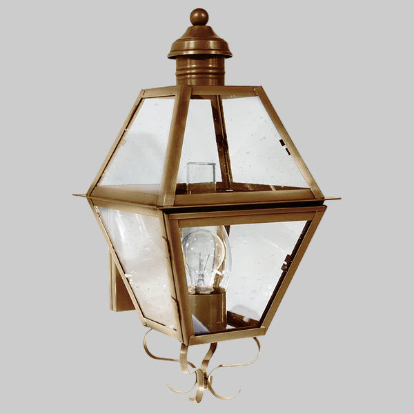 Decorative outdoor wall light fixture with brass finish and clear glass on a gray background