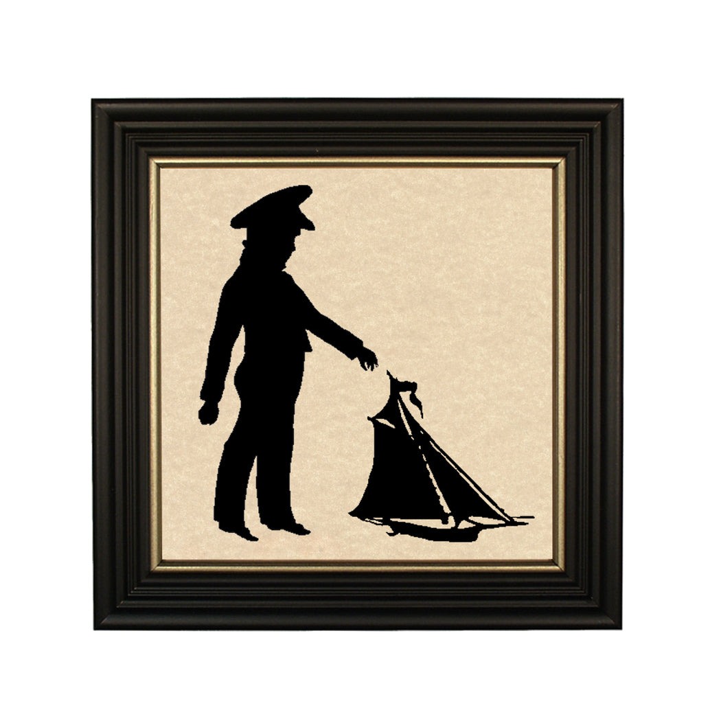 A paper cut silhouette of a boy with a pond boat, framed in a black solid ash wood frame with gold trim.