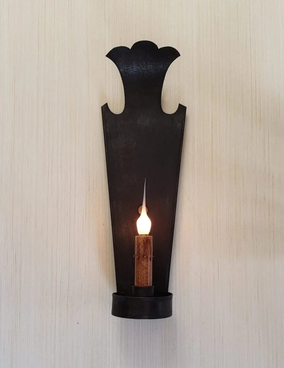 Black wall sconce with a candle on a textured white wall