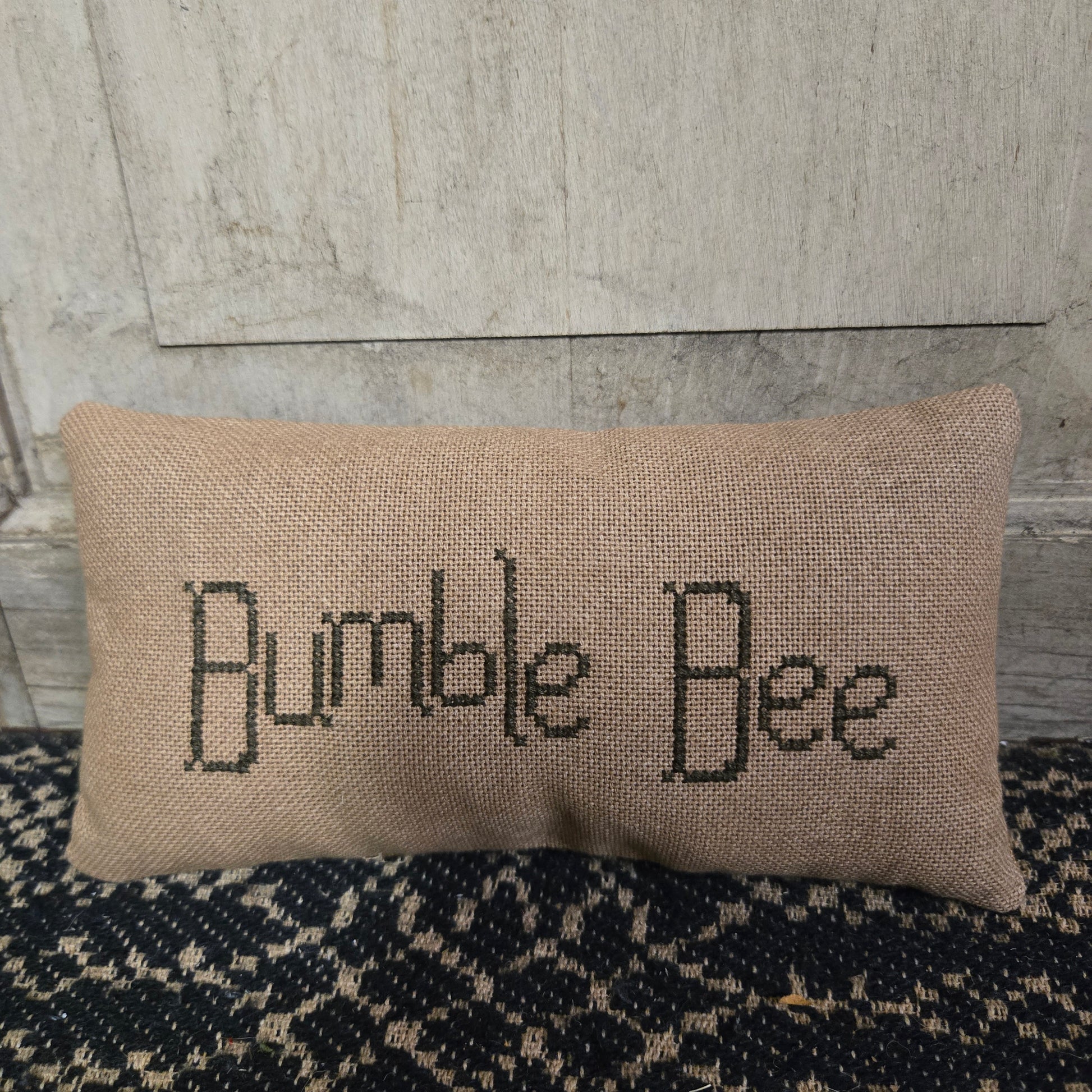 Beige pillow with 'Bumble Bee' text on a textured surface.