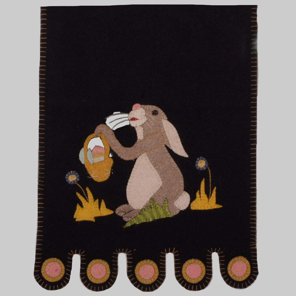 A black table runner with a whimsical bunny holding a basket in the center, surrounded by a floral motif.