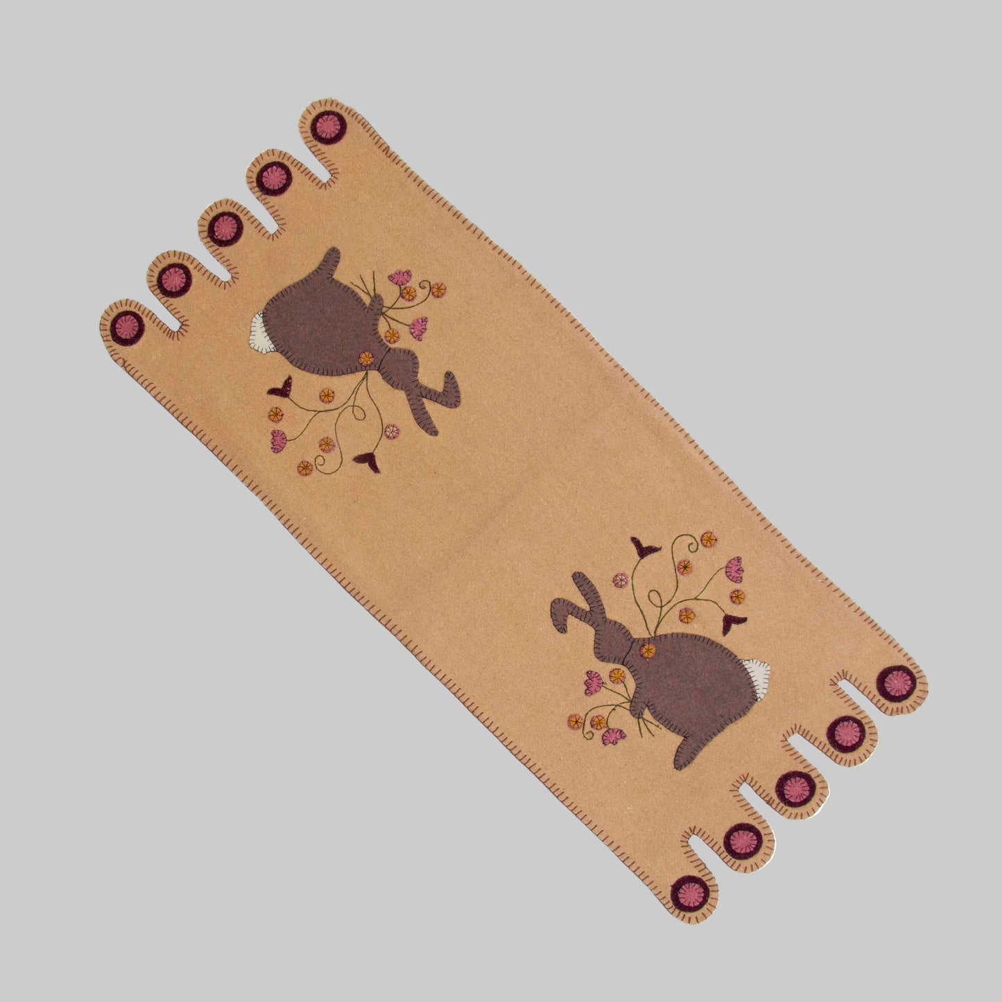 A beige table runner with a whimsical bunny design and floral elements, featuring decorative buttons at the corners.