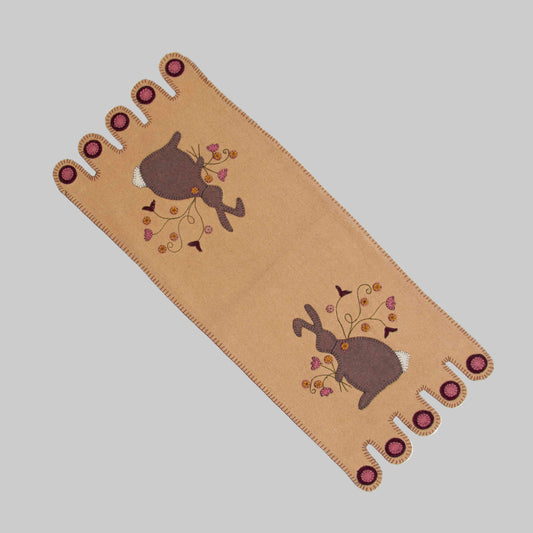 A beige table runner with a whimsical bunny design and floral elements, featuring decorative buttons at the corners.