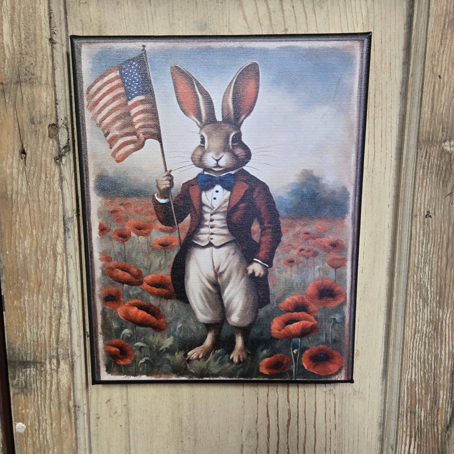 A canvas print featuring a stylized illustration of a rabbit dressed in a overcoat and holding a flag, set against a backdrop of a field with red poppies.