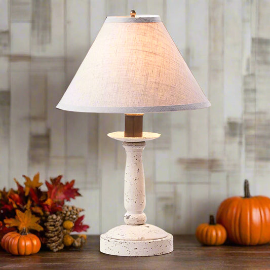 Table lamp with a white textured base and beige shade on a wooden surface with pumpkins and fall leaves.