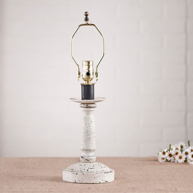Wooden lamp base with white paint on white background with daisies beside it