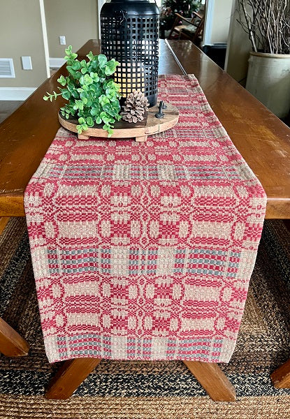 A red, green, and tan geometric patterned long table runner displayed on a wooden dining table.