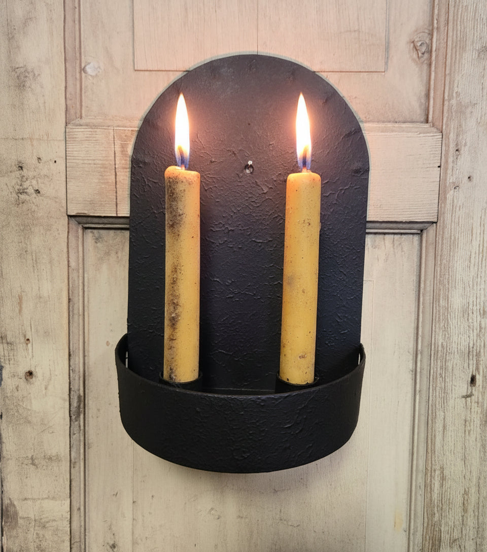 Black wall-mounted candle holder with two yellow candles on a wooden background