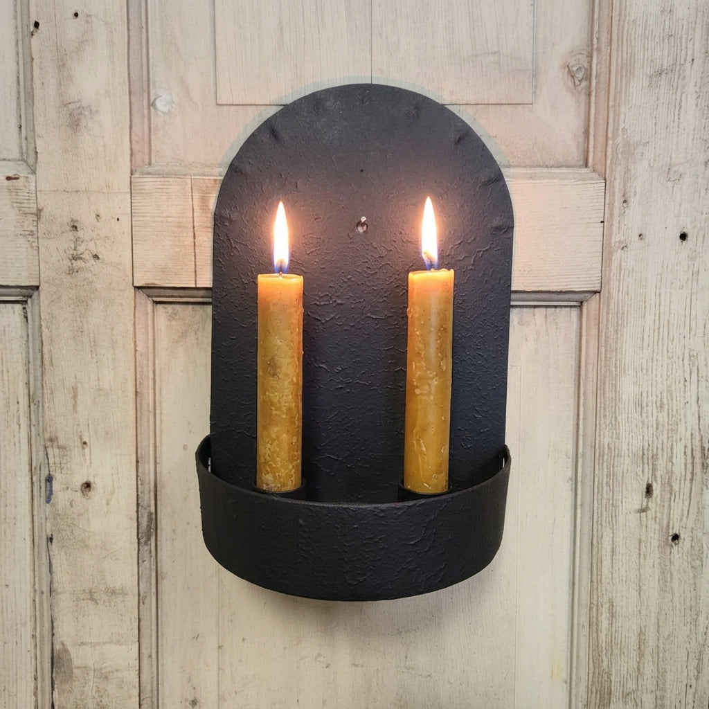 Black wall-mounted candle holder with two yellow candles on a wooden background
