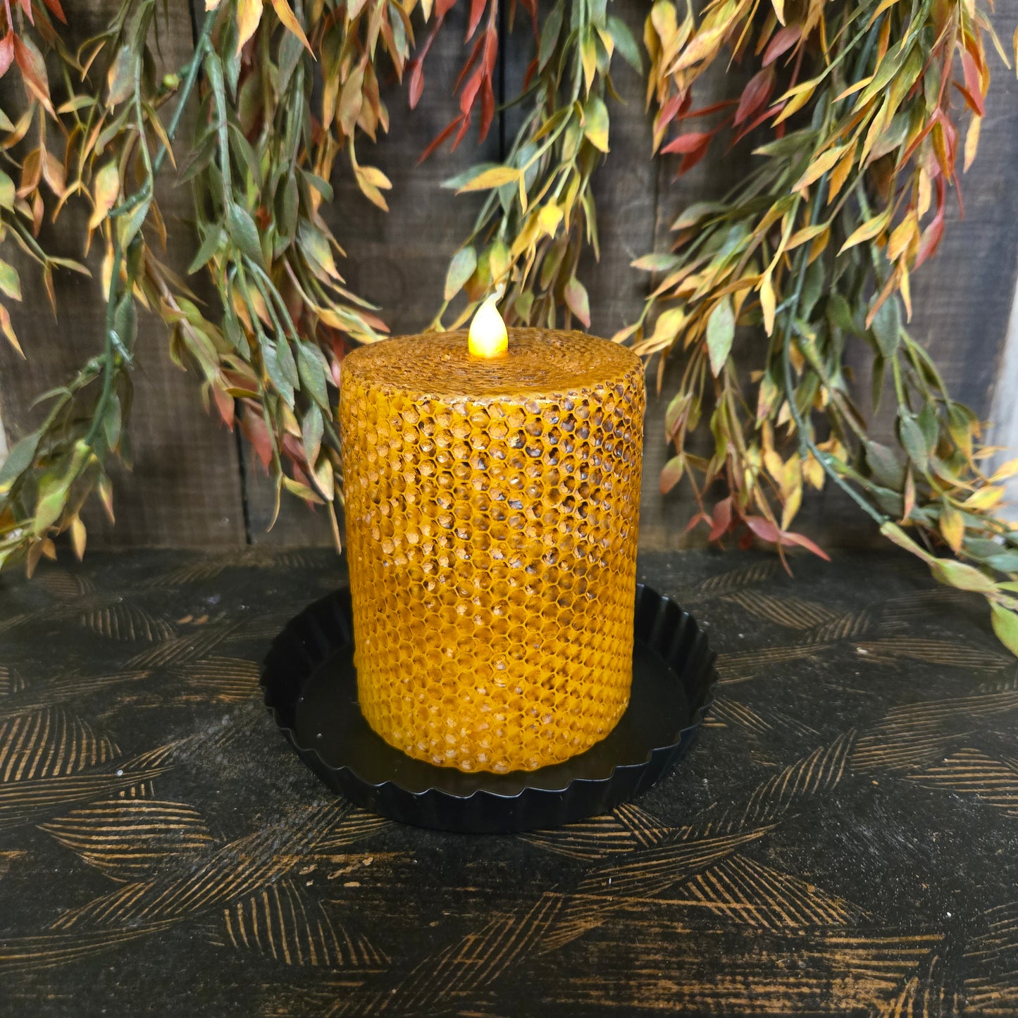 Yellow woven candle on black candle pan with greenery on a dark textured surface