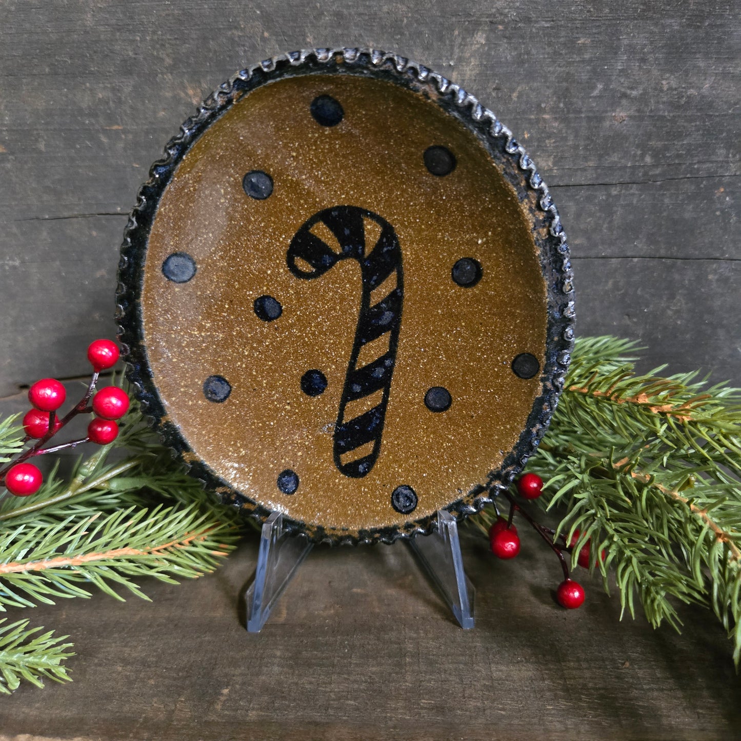 Decorative stoneware plate with candy cane design on a wooden surface with greenery and berries.