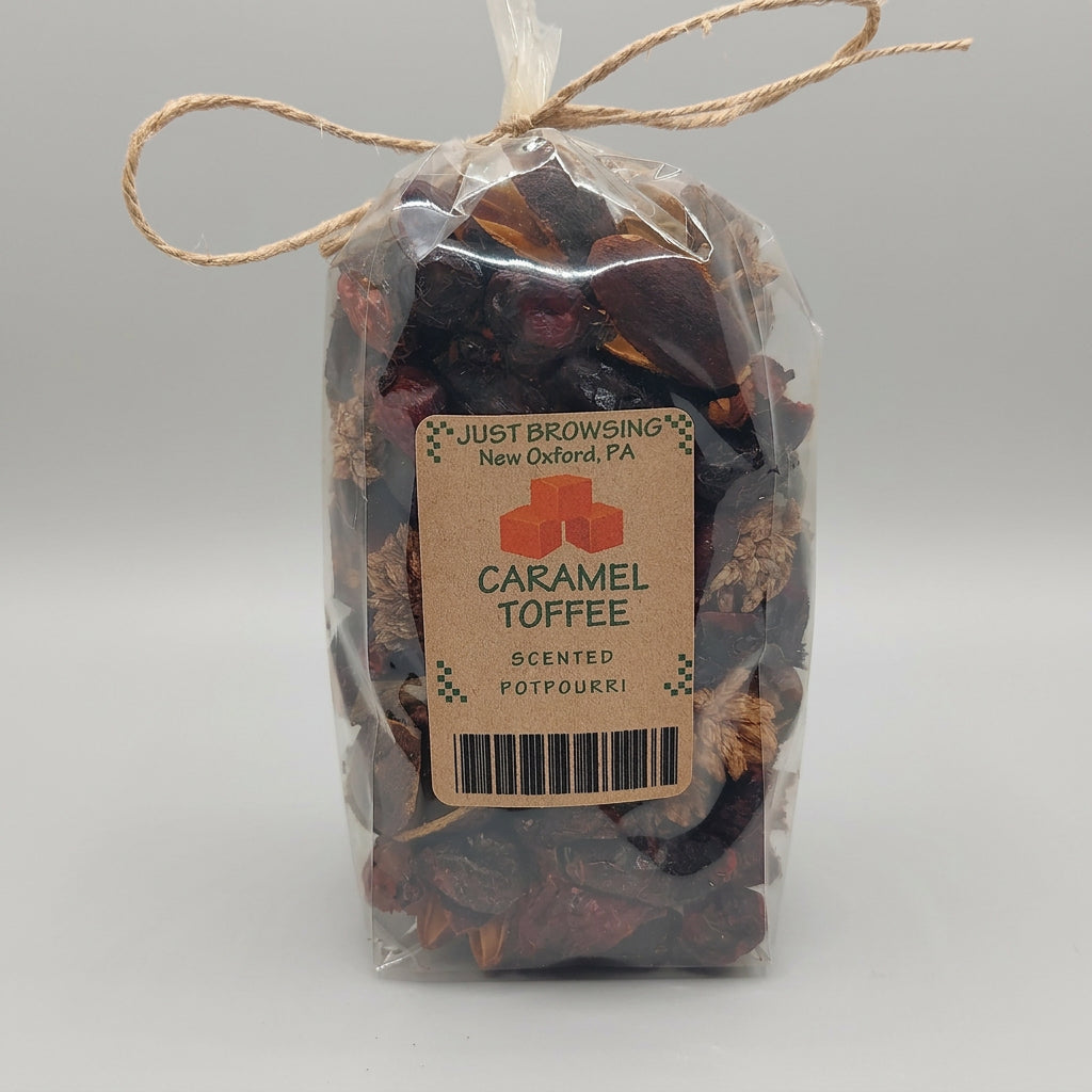 A clear plastic bag tied with twine, filled with dried botanicals and coffee pieces, featuring a cardboard label that reads 'Just Browsing New Oxford PA Caramel Toffee Scented Potpourri'.