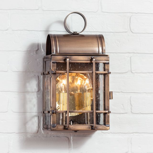 A solid weathered brass outdoor wall light with a 2-light design, hanging on a white brick wall.