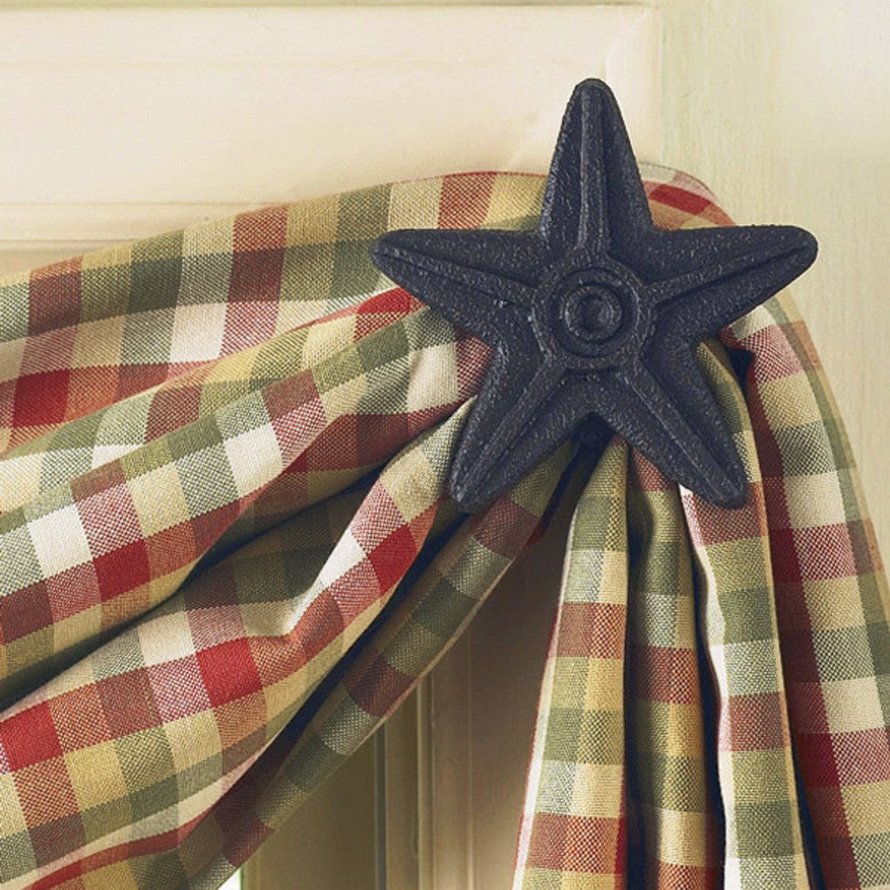 A black cast iron star-shaped curtain hook hanging from a curtain with a checkered pattern.