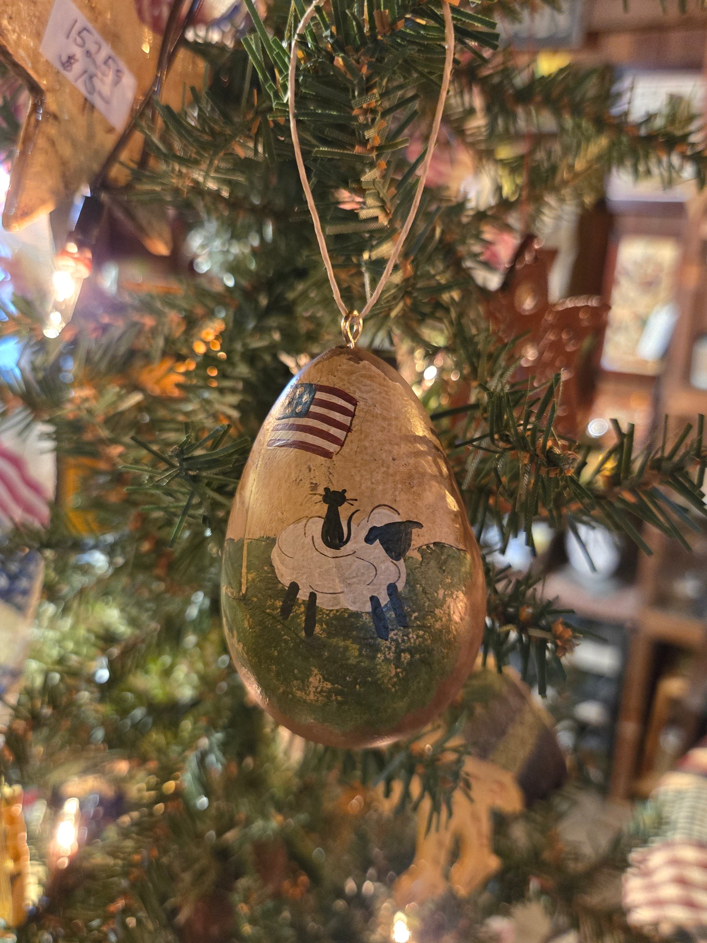 A handcrafted gourd ornament with a painting of a sheep and a flag, hanging on a Christmas tree.