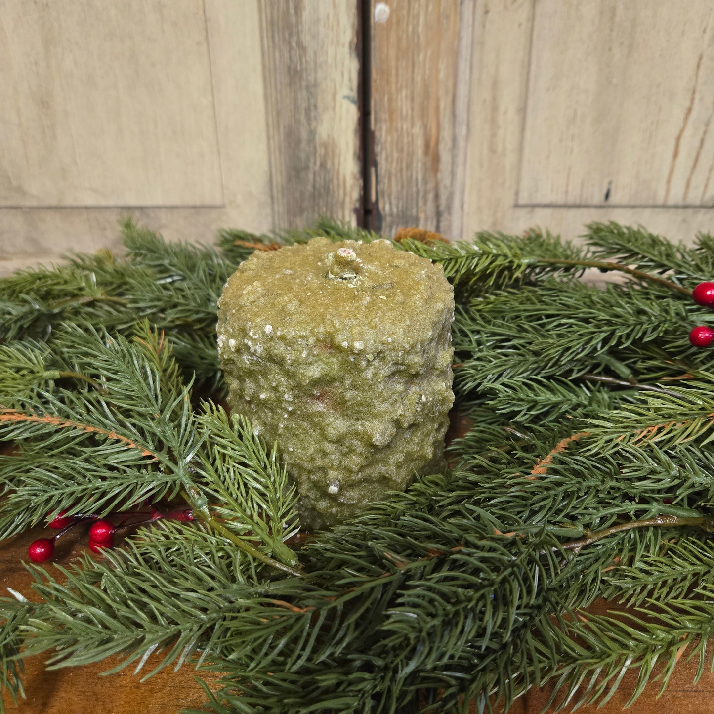 Cedar berry hearth candle on wood surface surrounded by greenery with berries