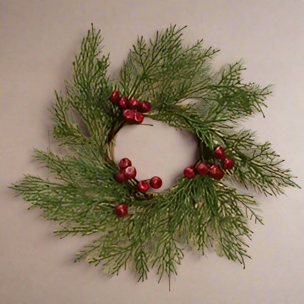 A round cedar wreath with green pine branches and red berries, placed on a wooden surface.