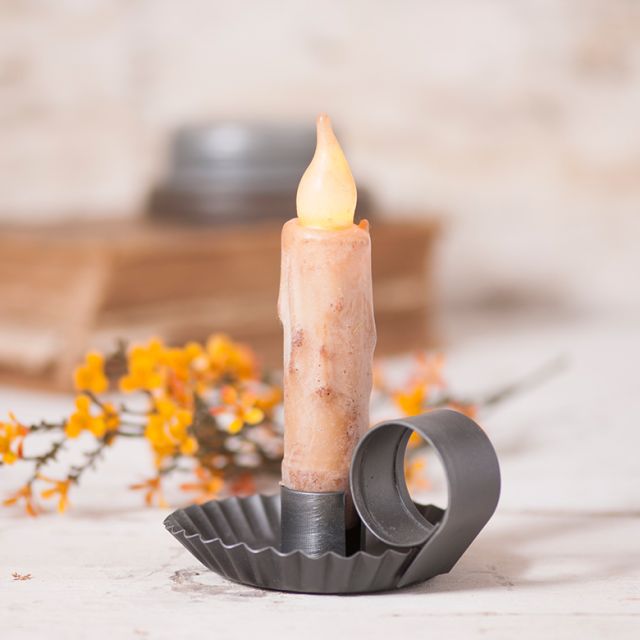 A smokey black chamberstick candle holder with a pewter brushed finish, displayed with a candle and decorative yellow flowers.