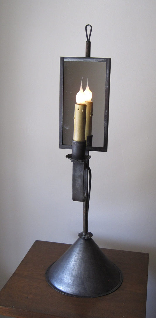 A tin table light with a mirrored light bulb encased in a metal holder, placed on a wooden surface against a white wall.
