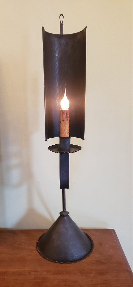 Decorative tin table light with a lit candle on a wooden surface.