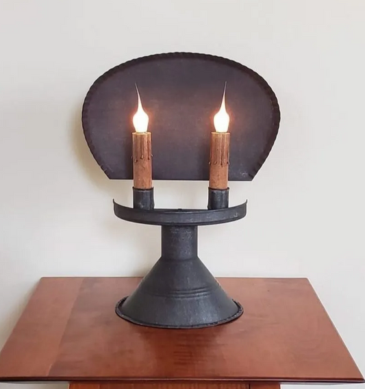 A Chesapeake Tin Table Light with two lit candles on a wooden surface, showcasing its sleek design and black color.