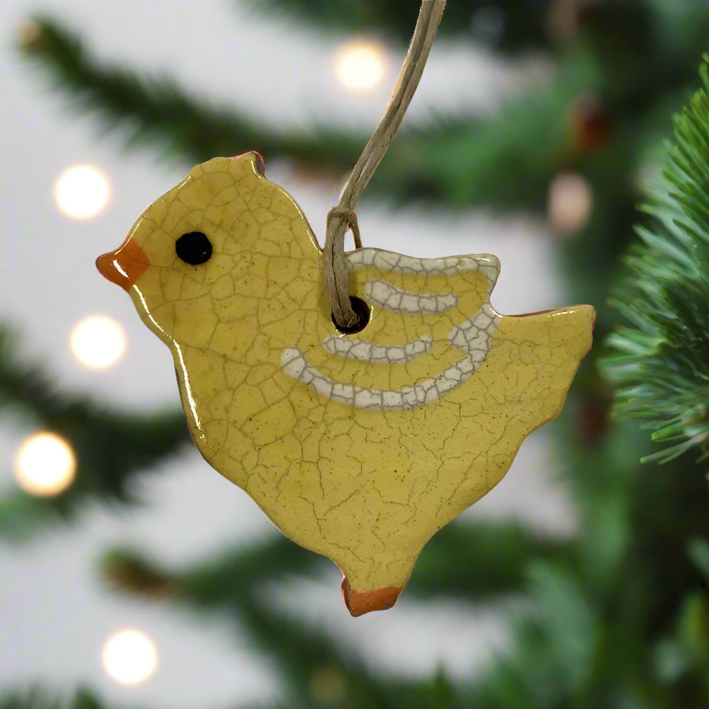 A handcrafted yellow chick redware ornament with a speckled pattern and black beak, attached to a cord for hanging.