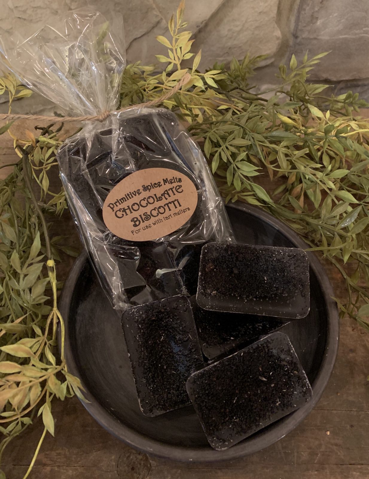 Packaging marked Chocolate Biscotti next to wax chunks in a bowl surrounded by green leaves