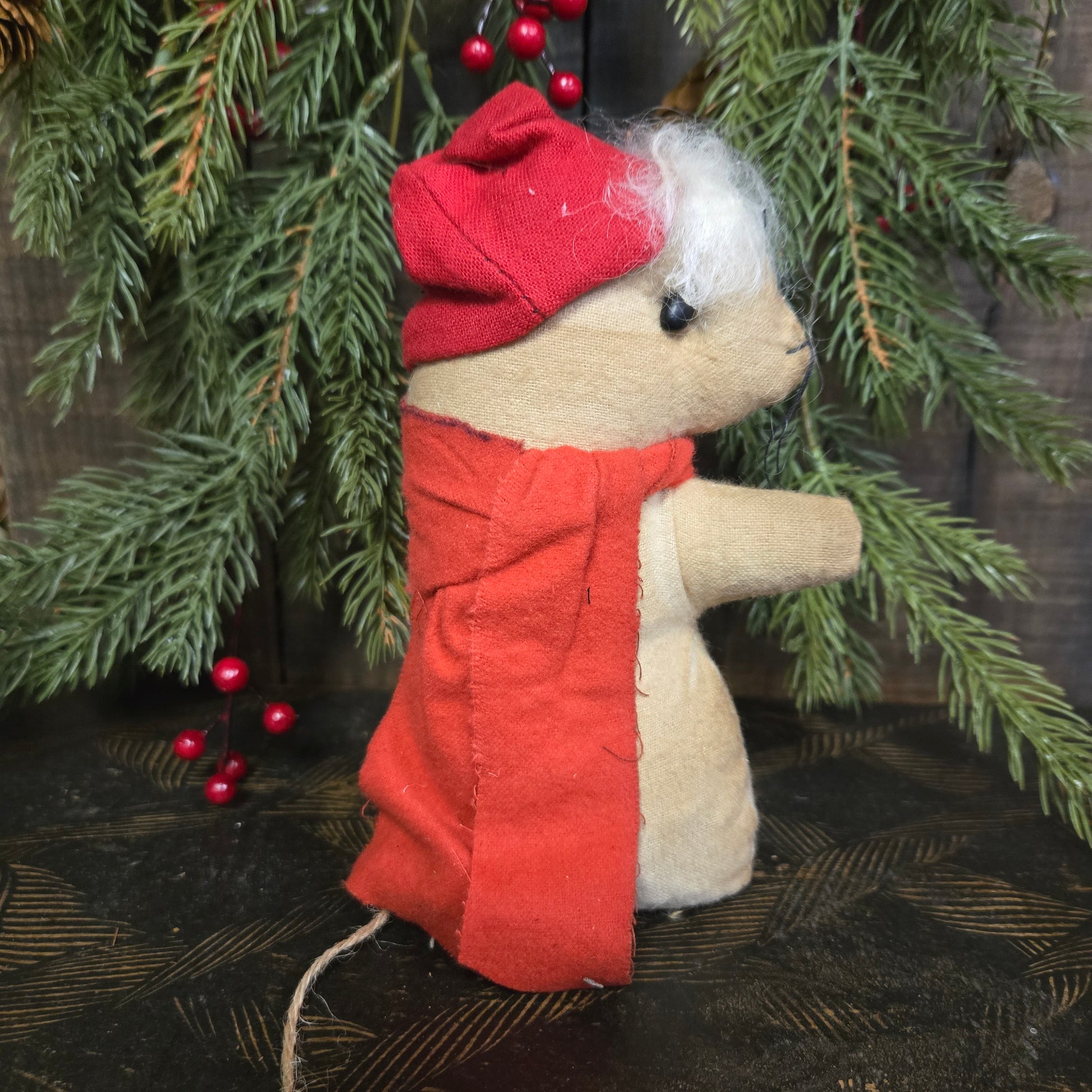 Small fabric dog toy in a red coat with greenery and berries in the background