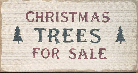 A wooden sign with 'Christmas Trees For Sale' text in red and green, mounted on a wooden wall.