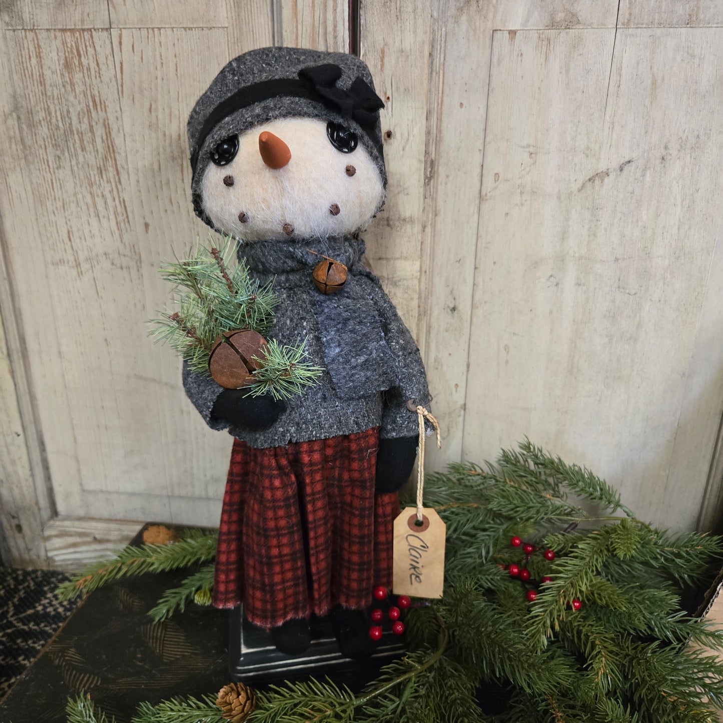 Decorative snowman with a tag labeled 'Claire' next to a wreath on a wooden surface