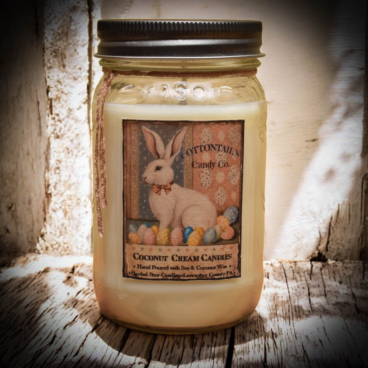 A mason jar candle with a label featuring an illustration of a rabbit and text that reads 'Coconut Cream Candies'.