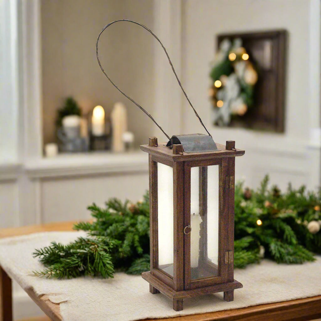 A rustic mango wood lantern with a metal wire handle and glass panels, designed in a colonial style.