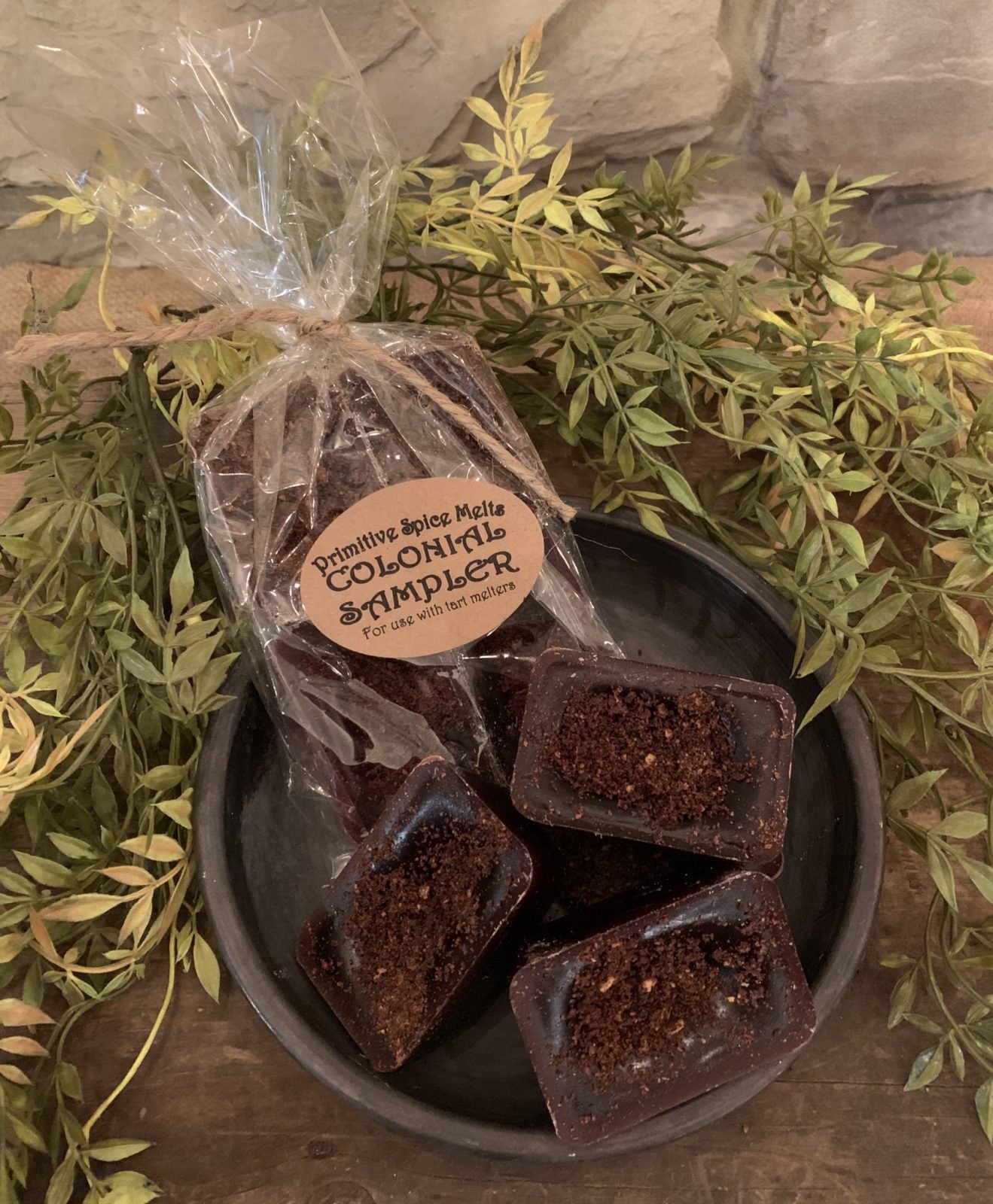 A pack of brown colored wax melts designed to resemble chocolate brownies, placed on a dish with greenery in the background.