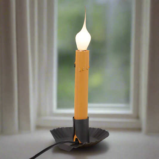 A smokey black window sill light with a yellow candle-like appearance, with a wire base and a switch on the cord.