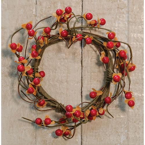 A round candle ring made of brown twigs with burnt orange berries and yellow accents, displayed against a wooden background.