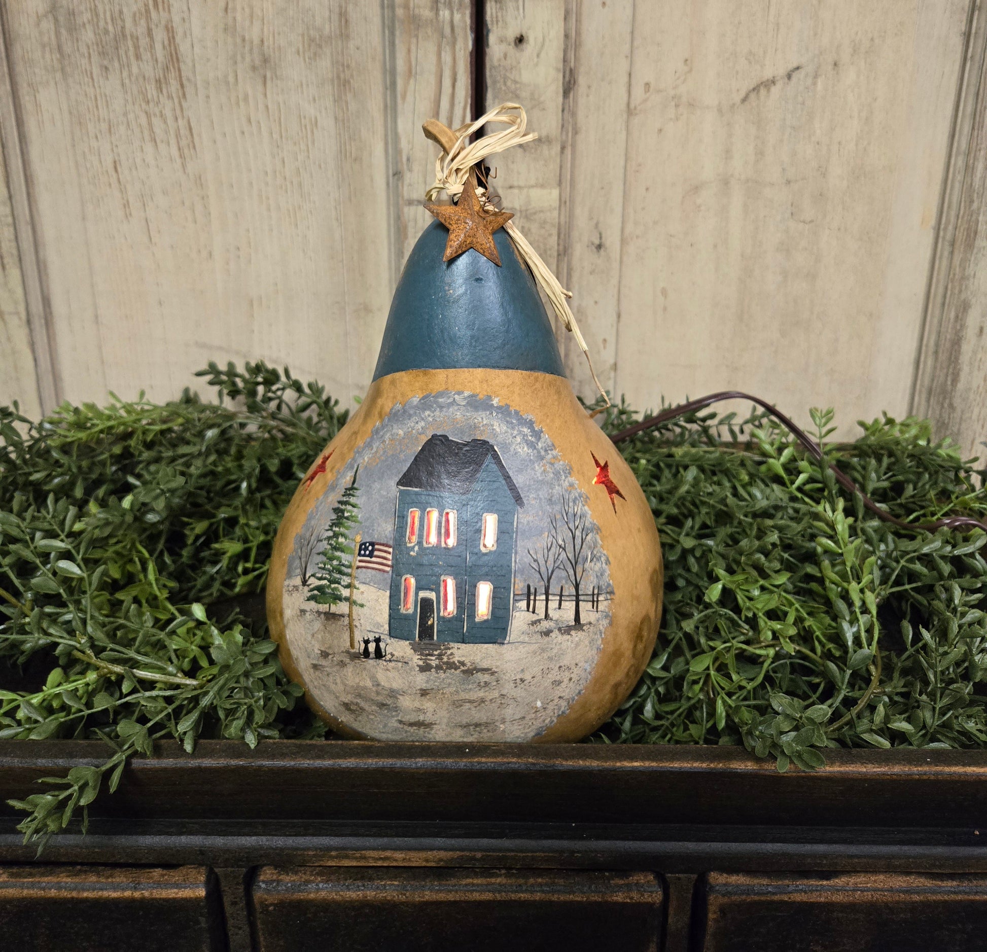 Hand-painted dried gourd with cutouts for light featuring a blue house and a Christmas tree