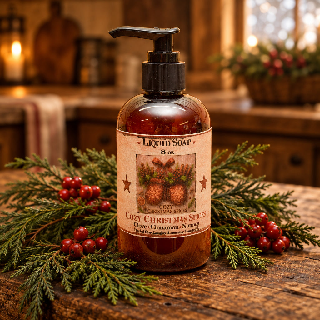 A 8 oz amber glass pump bottle of Cozy Christmas Spices liquid soap, featuring a black pump and a rustic beige label with pinecones and cinnamon sticks, set on a wooden surface with snow and a blurred Christmas tree in the background.