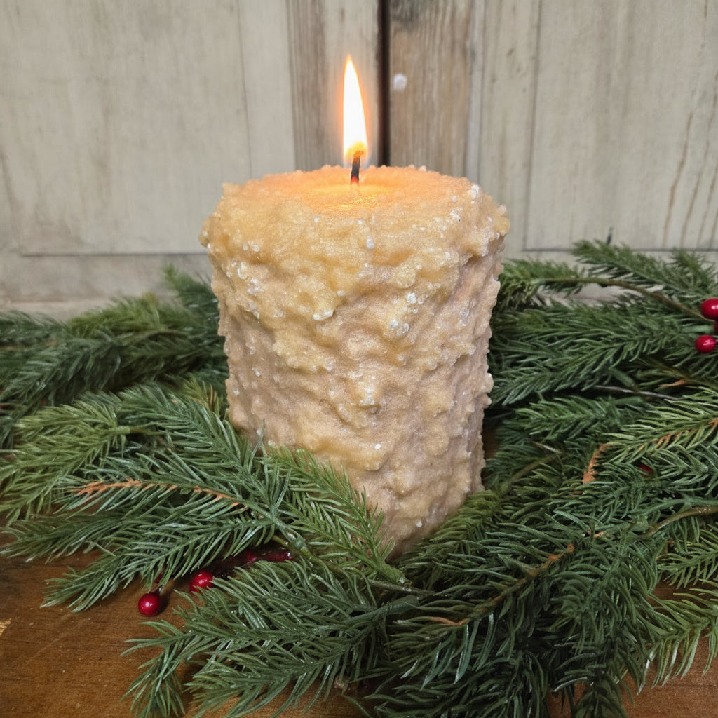 A large brown sugar candle with cranberry center, surrounded by green pine branches and red berries.