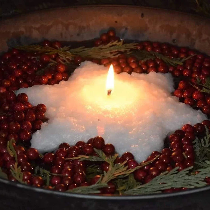 Star-shaped candle surrounded by red berries and greenery in a dark setting