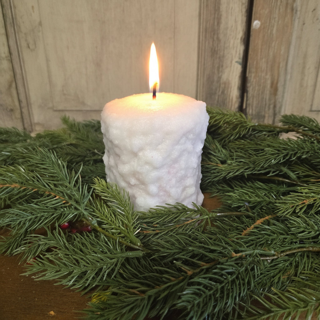 A small pillar-shaped cranberry sugar cookie with a frosting covering, placed on a surface with green pine branches and a rustic background.