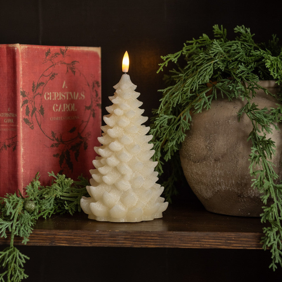 Decorative candle shaped like a Christmas tree on a shelf with a book and plant.